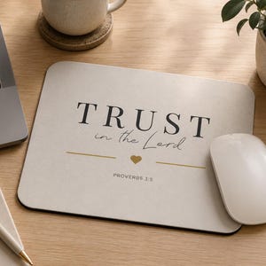 May include: A beige rectangular mousepad with the text "TRUST in the Lord" and "PROVERBS 3:5" in black. A gold heart and line are below the text. A white computer mouse is to the right of the mousepad.