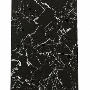 Pode incluir: Um painel retangular com uma superfície preta e um padrão de veios de mármore branco. O painel tem três orifícios circulares alinhados verticalmente ao longo do lado direito, proporcionando uma visão clara da textura escura e contrastante.