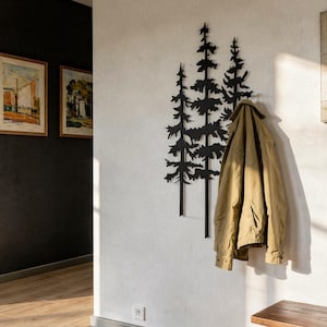 Pode incluir: Interior de um corredor com uma porta branca, uma parede escura e uma silhueta de árvore de metal preto numa parede branca. Um casaco bege está pendurado na parede. Um banco de madeira e um tapete estampado também são visíveis.