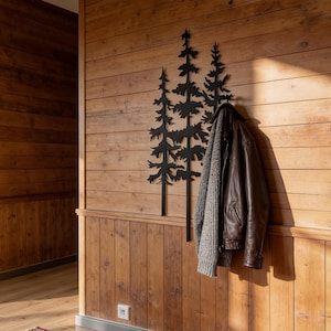 May include: A wooden wall with a decorative black metal tree design and a brown leather jacket hanging on it. The wall is made of horizontal wooden planks, and the floor is made of wood.