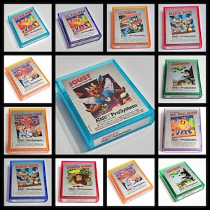 May include: A collection of Atari ProSystem game cartridges, including titles like Ms. Pac-Man, Mario Bros., and Joust. Each cartridge features colorful artwork and is encased in a clear plastic case. The games are from the 1980s.