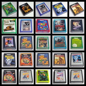 May include: A collection of twenty-five Atari 7800 video game cartridges in various colored plastic cases. The cartridges feature diverse cover art, including titles like Tank Command, Klax, Basketbrawl, Motor Psycho, Mean 18, and Q-bert.