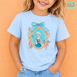 A young girl wearing a light blue t-shirt with a picture of a character from the Disney movie Frozen.