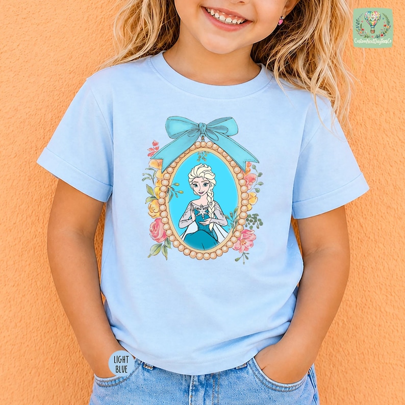 A young girl wearing a light blue t-shirt with a picture of a character from the Disney movie Frozen.