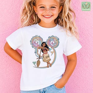 A young girl with blonde hair is smiling and posing in front of a pink wall. She is wearing a white t-shirt with a colorful graphic of a character from Disney.