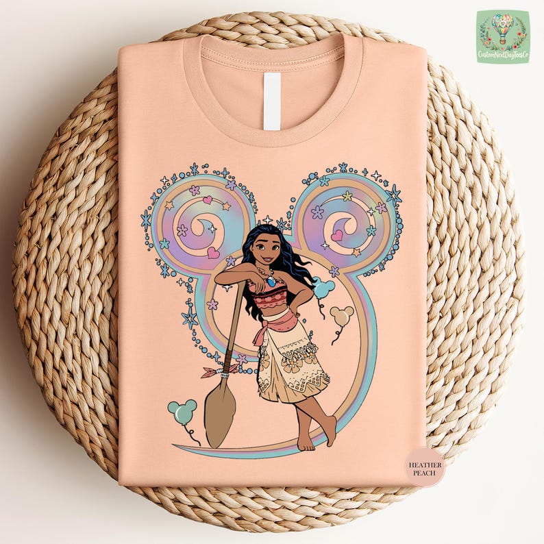 A t-shirt with a cartoon illustration of a young girl with dark hair and a colorful skirt, holding a broom and surrounded by whimsical elements such as flowers and swirls.