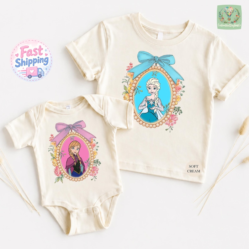 two white t-shirts with illustrations of two female characters from the Disney movie Frozen, one larger and one smaller. The larger t-shirt has a blue bow around the neckline, while the smaller t-shirt has a pink bow. The t-shirts are displayed on a white background, and there are some dried flowers and a shipping label visible in the top left corner.