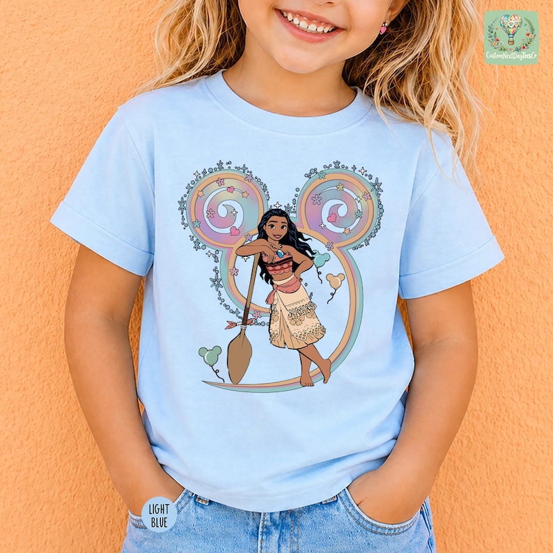 A young girl wearing a light blue t-shirt with a Disney character printed on it.