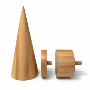 May include: A light brown wooden cone standing upright next to a thin wooden disc and a thicker wooden cylinder, both of which feature a small protruding wooden peg on their side, showcasing a natural wood grain finish throughout the set.