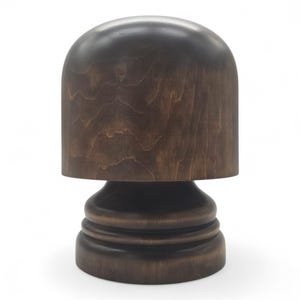 Może przedstawiać: Ciemnobrązowy drewniany stojak na kapelusze z gładką, zaokrągloną kopułą na górze i stopniowaną, okrągłą podstawą. Słoje drewna są widoczne na całej powierzchni, ukazując naturalne wzory w głębokim, polerowanym wykończeniu o solidnej budowie.