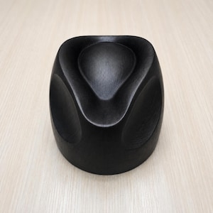 May include: A solid black wooden object with a smooth, rounded, and sculptural form. The piece features a deep, central teardrop-shaped indentation on the top surface, surrounded by curved, concave sides that create a symmetrical, organic shape.