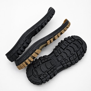 May include: Three black and tan rubber shoe soles featuring a deep, aggressive lug tread pattern. The soles are arranged in a cluster, showing the bottom surface with textured grip blocks and a durable, thick construction for footwear repair.