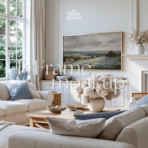 Op de afbeelding: Een rechthoekige goudkleurige lijst met een landschapsschilderij van heuvels en blauwe bloemen, gemonteerd aan een witte muur boven een witte kast. De tekst The Mossy Mockups en TvFrame mockup staat in witte letters over de afbeelding.