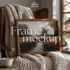 Könnte beinhalten: Ein gerahmter Landschaftskunst-Druck mit Holzrahmen, der auf einer grob gestrickten Decke liegt. Das Kunstwerk zeigt eine Flussszene mit Bäumen und Schilf. Der Text "Frame mockup" ist über dem Bild überlagert, zusammen mit einem PSD-Dateisymbol.
