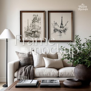 May include: Two rectangular wall frames with dark brown borders containing black and white ink sketches of Parisian street scenes featuring the Eiffel Tower. The frames are displayed above a beige sofa with assorted pillows and a throw blanket.