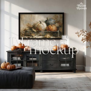 May include: A black TV frame mockup with a painting of pumpkins and fall leaves. The scene includes a dark gray cabinet with pumpkins, candles, and a gray ottoman. The text "Tv Frame mockup" is overlaid on the image.