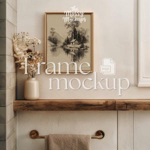 May include: A framed landscape art print with a gold frame hangs above a wooden shelf. A beige vase with dried flowers sits on the shelf. A towel hangs from a brass towel bar. The words "Frame Mockup" are displayed.
