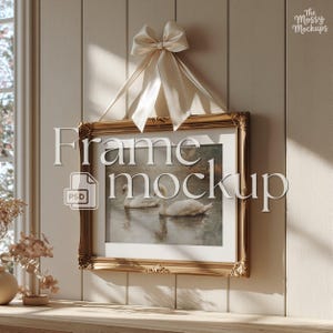 May include: A rectangular gold-toned ornate picture frame hanging from a cream-colored satin ribbon bow. The frame contains an image of two white swans swimming on water. The text "Frame mockup" and "PSD" are overlaid on the image.