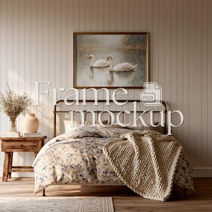 May include: A bedroom scene with a bed dressed in floral bedding, a cream knitted throw, and a framed swan painting. A small wooden bedside table holds a vase and dried flowers. The wall is panelled.
