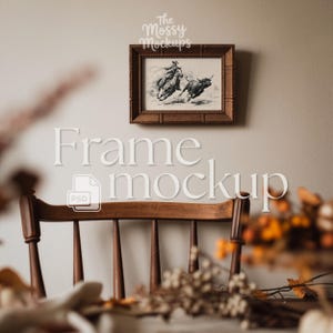 May include: A framed black and white illustration of a cowboy riding a bull, displayed on a neutral wall. The frame is a dark brown colour. The image is a frame mockup with the text "Frame mockup" and "The Mossy Mockups".