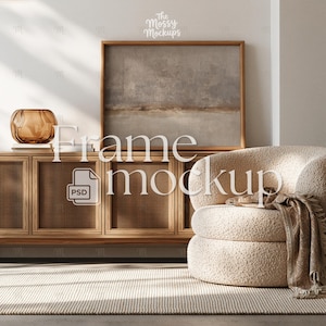 May include: A framed artwork with a neutral landscape painting hangs above a wooden cabinet with a woven front. A cream boucle armchair and a patterned throw blanket are next to the cabinet. The image includes the text "Frame mockup" and "The Mossy Mockups".