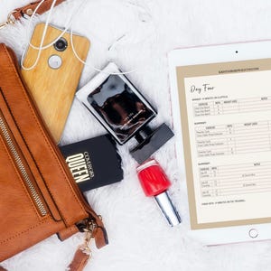 May include: A flat lay featuring a brown leather purse, a smartphone, a black perfume bottle, a black compact with "QUEEN" text, red nail polish, and a tablet displaying a workout plan. The items are arranged on a white, fluffy surface.