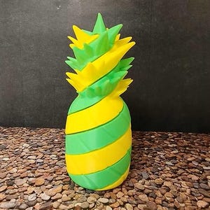 May include: A pineapple-shaped object featuring a spiraling, segmented design with alternating bright yellow and vibrant green horizontal bands. The top section consists of pointed, leaf-like protrusions in matching yellow and green colors.
