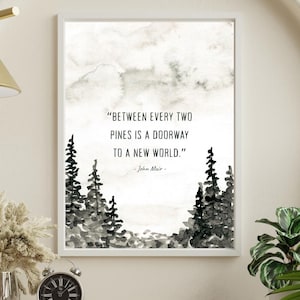 May include: A framed wall art print featuring a watercolor illustration of black pine trees at the bottom and the quote: "BETWEEN EVERY TWO PINES IS A DOORWAY TO A NEW WORLD." - John Muir - in black text against a white background.