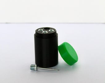 May include: A black cylindrical container with a green lid and a metal inflation needle. The top of the container features three circular openings with silver-colored metal inserts, designed to hold the needle securely when not in use.