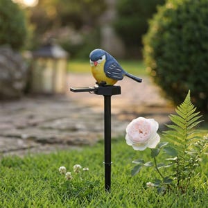 以下が含まれることがあります： 青、黄、白の鳥のフィギュアが乗ったソーラー式ガーデンライト。鳥には小さな赤い嘴があり、屋外照明として地面に差し込める細い黒い金属製のポールに取り付けられています。