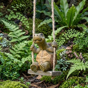 May include: A brown, textured turtle figurine sitting on a small, rectangular wooden swing suspended by two thick, light-colored jute ropes. The turtle has a detailed shell pattern, visible limbs, and a smiling expression, hanging in a garden.
