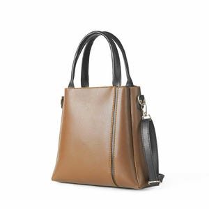 May include: A structured brown handbag with a smooth finish, featuring two black top handles and a detachable black shoulder strap. The bag has a vertical black accent line on the front panel, gold-toned metal hardware, and a tapered silhouette.