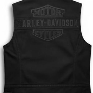 Puede incluir: Chaleco negro sin mangas con el logotipo de Harley-Davidson en relieve en la espalda. El logotipo incluye las palabras "MOTOR HARLEY-DAVIDSON CYCLES" en un diseño estilizado. El chaleco tiene un cierre de botón en la parte inferior.