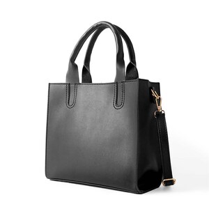 May include: A structured black handbag with a smooth finish, featuring two top handles and a detachable shoulder strap with gold-toned metal hardware. The bag has a rectangular silhouette with reinforced stitching at the handle attachments.