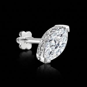 May include: A marquise-cut diamond stud earring with a halo of smaller diamonds. The earring has a silver post and a flower-shaped backing. The diamond is clear and sparkling, set against a black background.