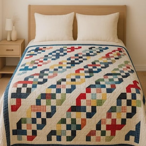 May include: A handmade quilt with a white background and diagonal rows of colorful, geometric blocks. The blocks feature red, blue, green, and yellow squares. The quilt has a dark blue border and is placed on a bed with white pillows.