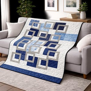 Peut inclure: Une couverture matelassée avec un motif géométrique dans les tons de bleu, gris et blanc. Le motif présente des carrés et des rectangles, créant une esthétique moderne. La couverture est drapée sur un canapé gris.