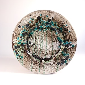 May include: A ceramic plate with a textured surface and a unique design. The plate features a brown and white base with accents of teal and black. The design includes speckled patterns and dripped lines, creating an artistic and handcrafted appearance.