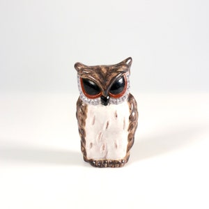May include: A ceramic owl figurine with a brown and white body, black eyes, and red and silver accents. The owl is standing upright and has a detailed, textured appearance. The figurine is a decorative item.