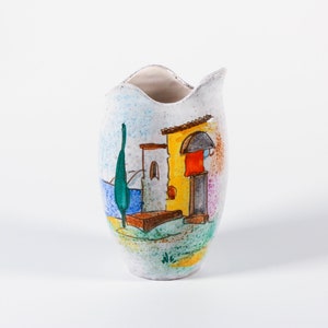 Puede incluir: Un jarrón de cerámica blanca con un borde ondulado, que presenta una escena pintada a mano de un edificio amarillo con una puerta roja, un árbol verde y agua azul.