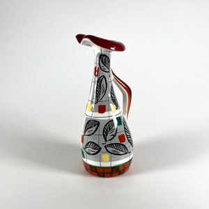 May include: A white ceramic jug with a red, green and yellow geometric pattern. The jug has a wide, flat spout and a handle.