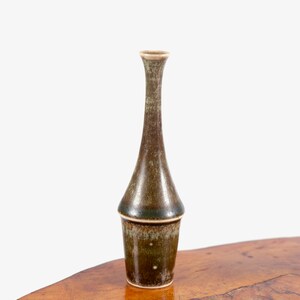 Puede incluir: Un peque&ntilde;o jarr&oacute;n de cer&aacute;mica verde oscuro con cuello estrecho y base redondeada. El jarr&oacute;n tiene un esmalte moteado y un borde marr&oacute;n claro.