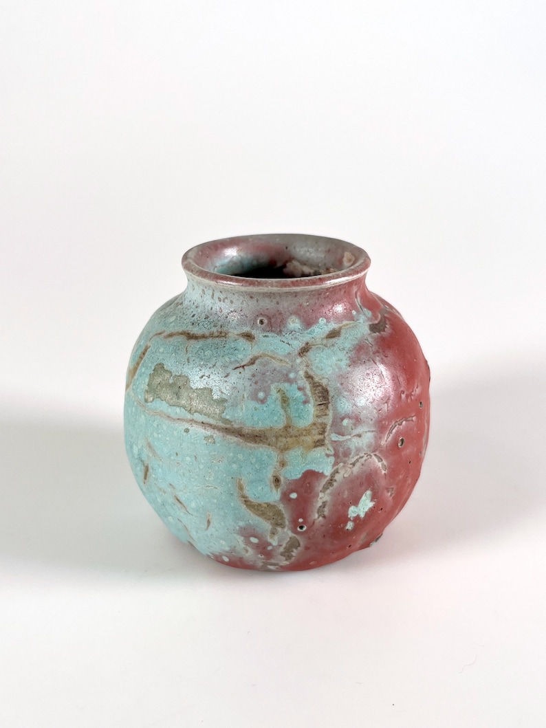 May include: A small, round ceramic vase with a mottled glaze in shades of blue, green, and red.