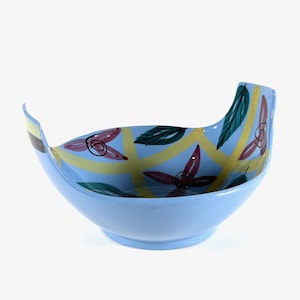 以下が含まれることがあります： ユニークなボート型のライトブルーのセラミックボウル。内側には、赤い花、緑の葉、黄色のストライプのフローラルパターンがあります。ボウルは滑らかで光沢のある仕上がりで、盛り付けに適しています。