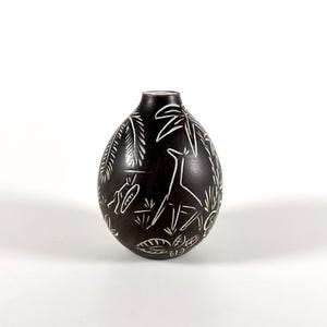May include: A black ceramic vase with a white design of stylized plants and animals. The vase has a rounded, egg-shaped body.