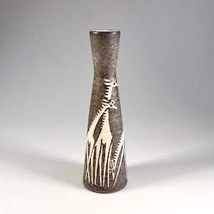 May include: A tall, slender vase with a dark brown, textured finish. The vase features a white giraffe and grass design. The vase has a flared base and a narrow neck. The vase is approximately 10 inches tall.