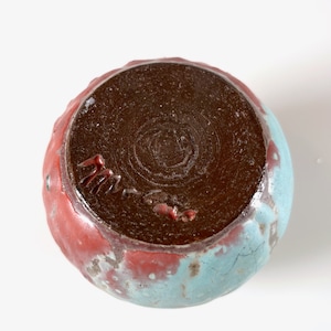 May include: A small, round ceramic bowl with a brown glaze on the inside and a blue and red glaze on the outside. The bowl has a signature on the bottom.