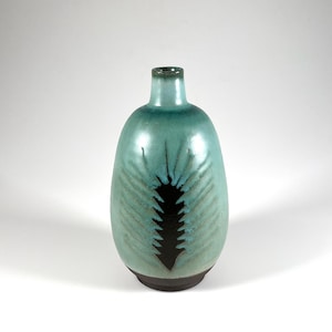 May include: A teal ceramic vase with a dark brown base and a black fern design. The vase has a rounded body and a narrow neck. The fern design is centered on the front of the vase.