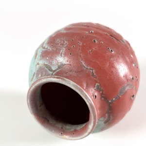 May include: A red and blue ceramic vase with a textured surface and small holes. The vase is tilted on its side, revealing the inside.