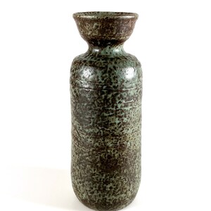 K&ouml;nnte beinhalten: Eine hohe, zylindrische Keramikvase mit einem gesprenkelten gr&uuml;n-braunen &Uuml;berzug. Die Vase hat eine leicht ausgestellte &Ouml;ffnung oben.